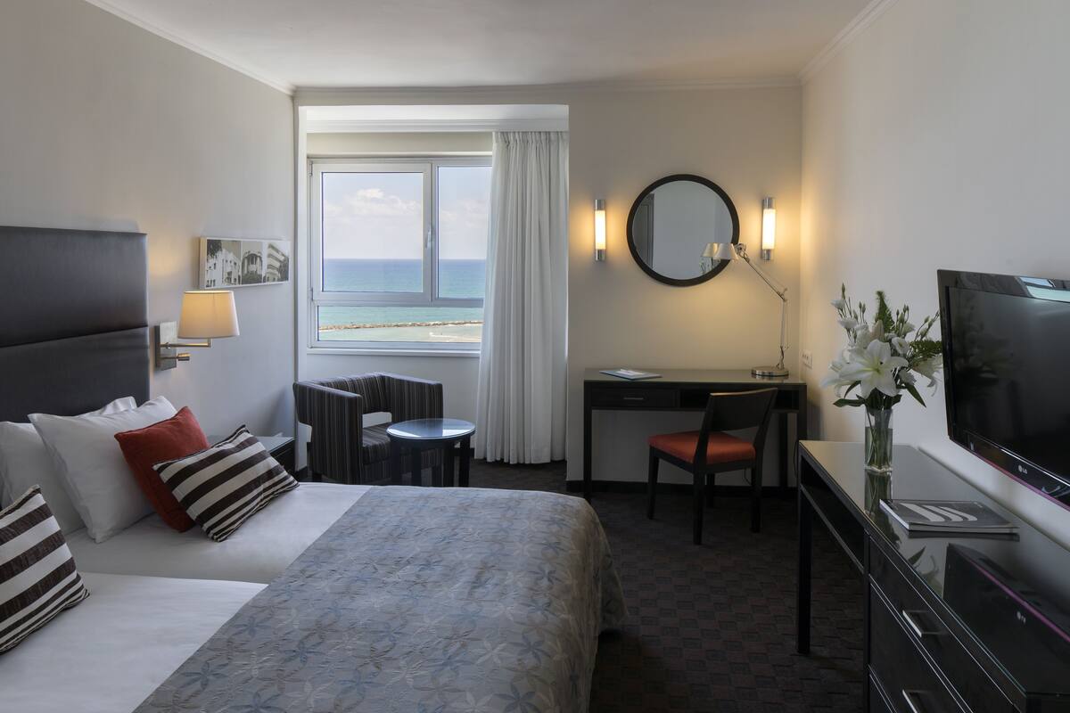 A hotel room with a bed, a desk, a chair, a TV, and a view of the ocean.