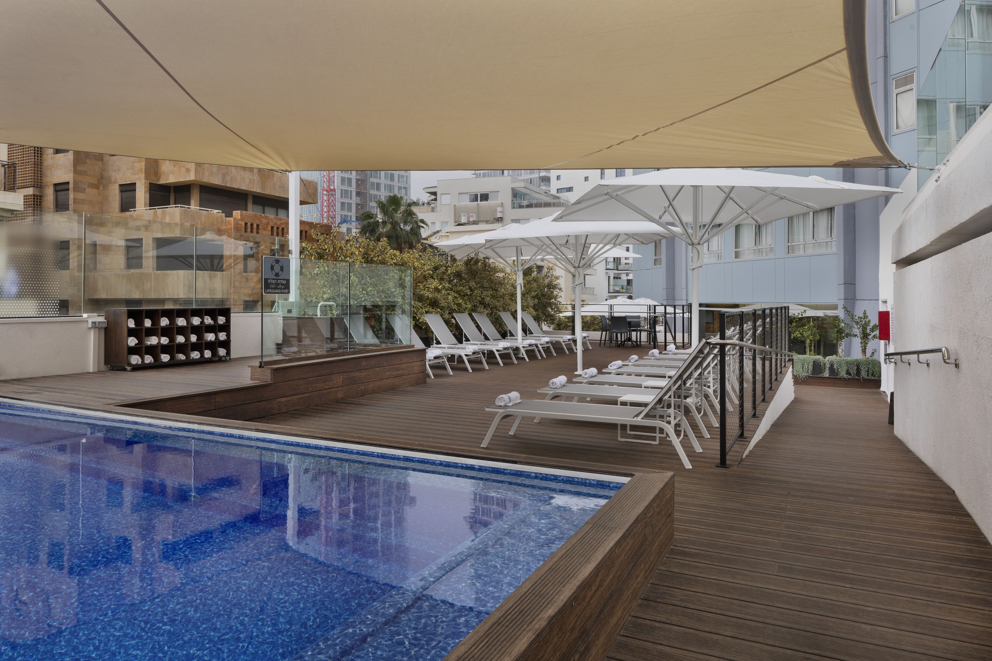A rooftop pool area with lounge chairs, umbrellas, and a glass enclosure with decorative items.