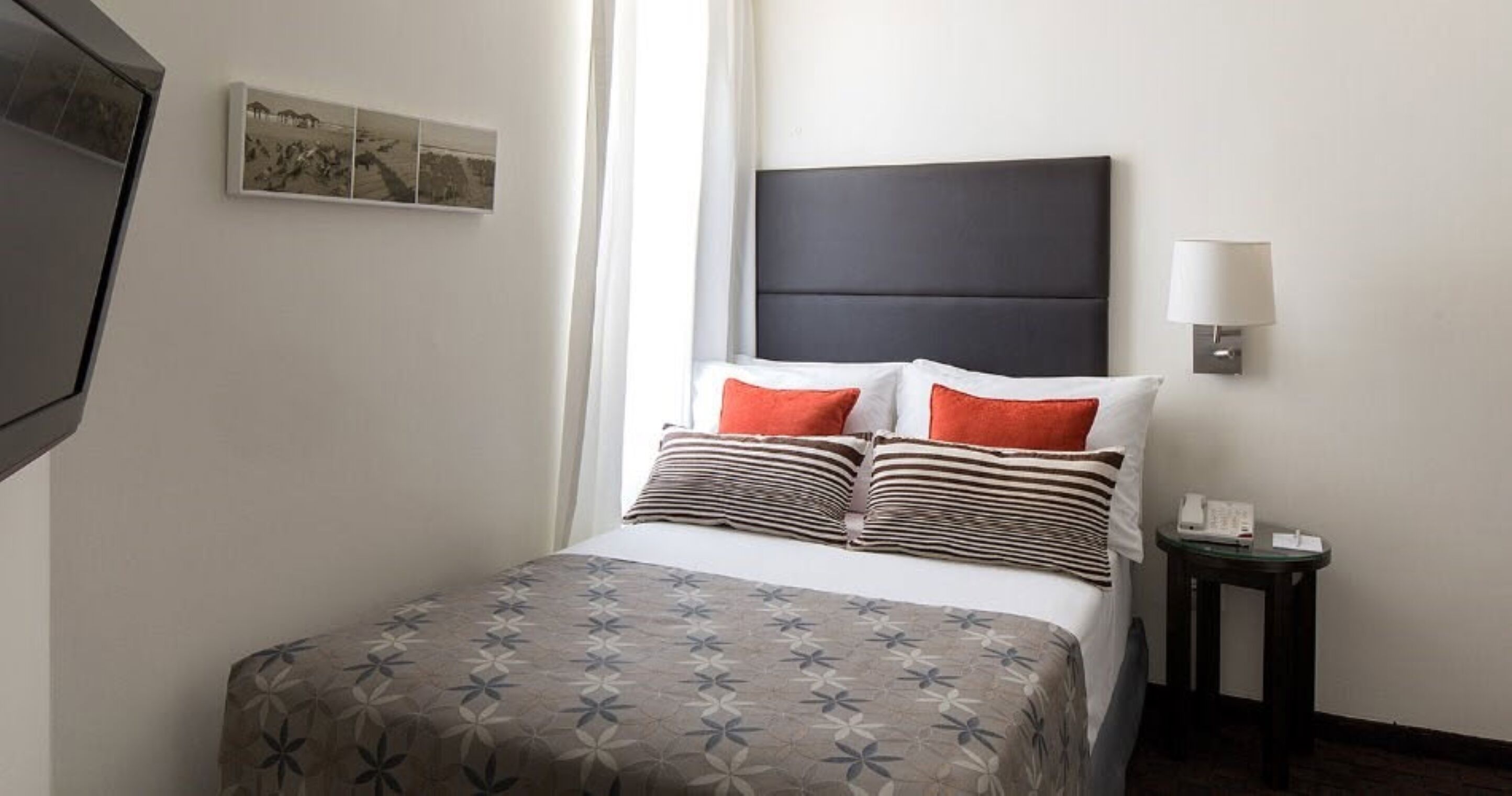 Une chambre d’hôtel avec un lit, une table de chevet, une lampe et un tableau accroché au mur.