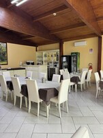 Zona pranzo con sedie e tavoli bianchi, una cucina sullo sfondo e un frigorifero Heineken.