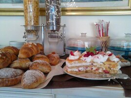 Una selezione di pasticcini e dolci in mostra, tra cui croissant, una torta con panna montata e fragole, e una macchina per caffè.