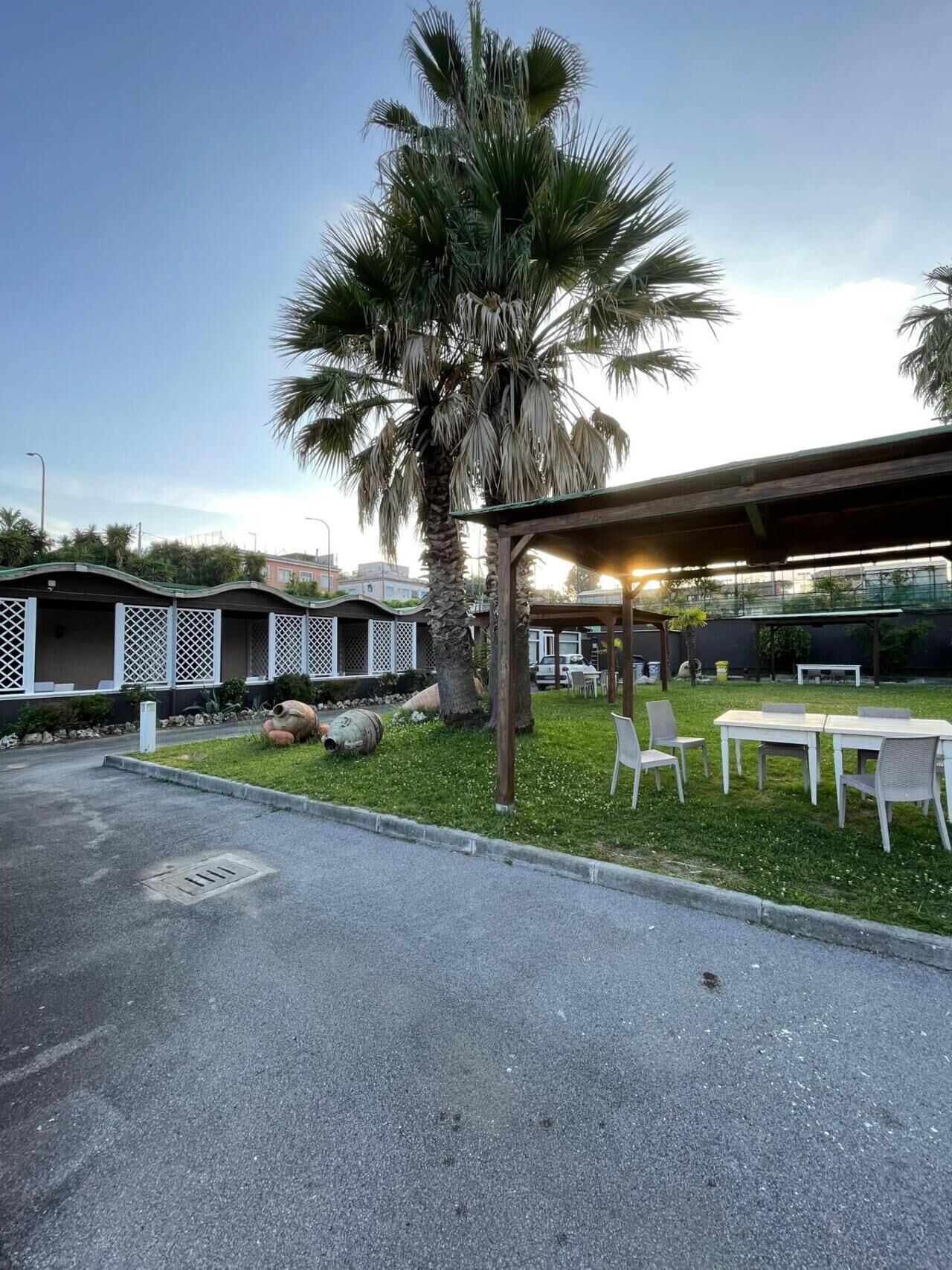 Un estacionamiento con un área de estar al aire libre techada, palmeras y un edificio con fachada de celosía.