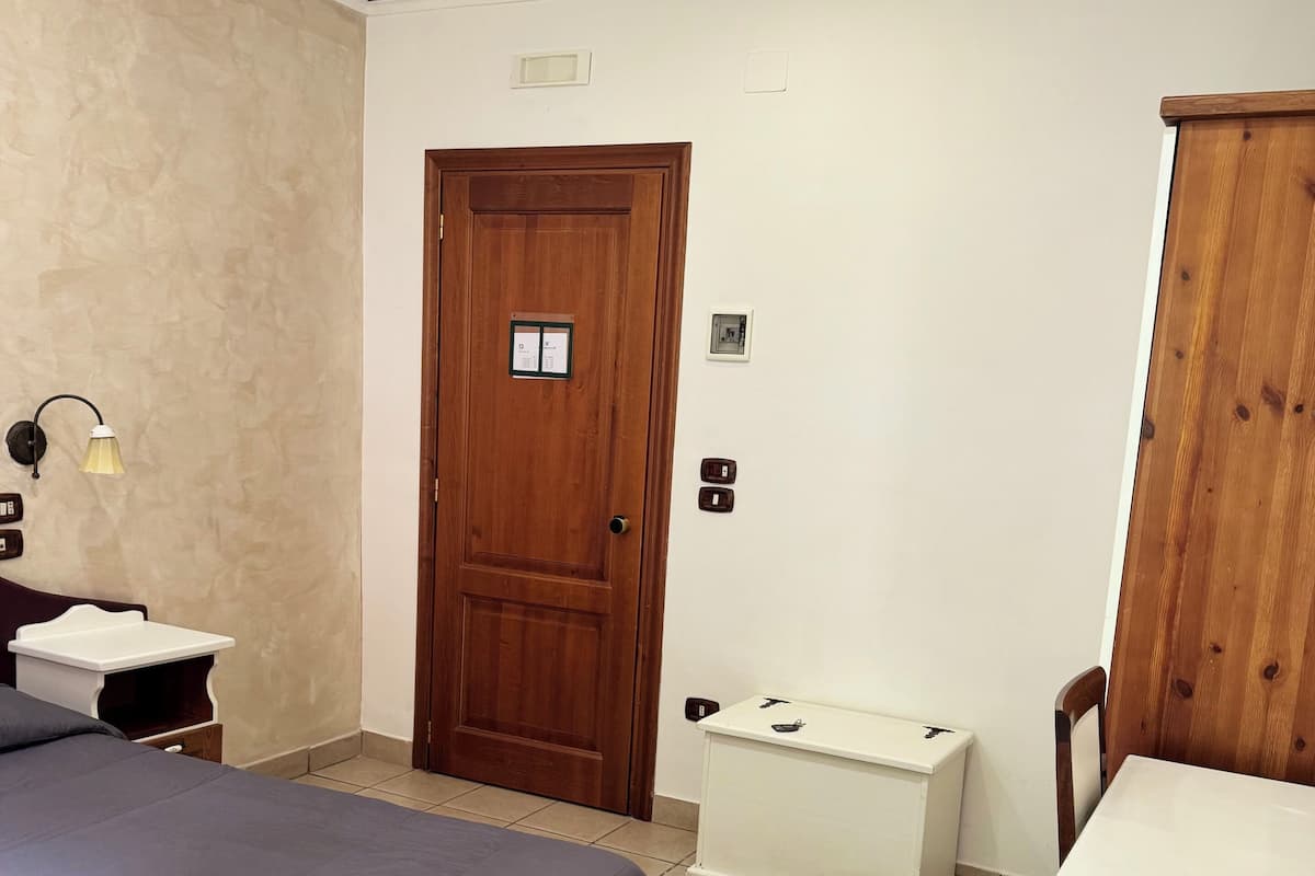 A bedroom with a bed, bedside table, lamp, wardrobe, and a door with a lock.