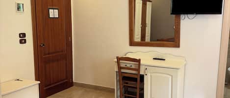 A bedroom with a bed, a wooden desk with a chair, a mirror, a television, and an air conditioning unit.