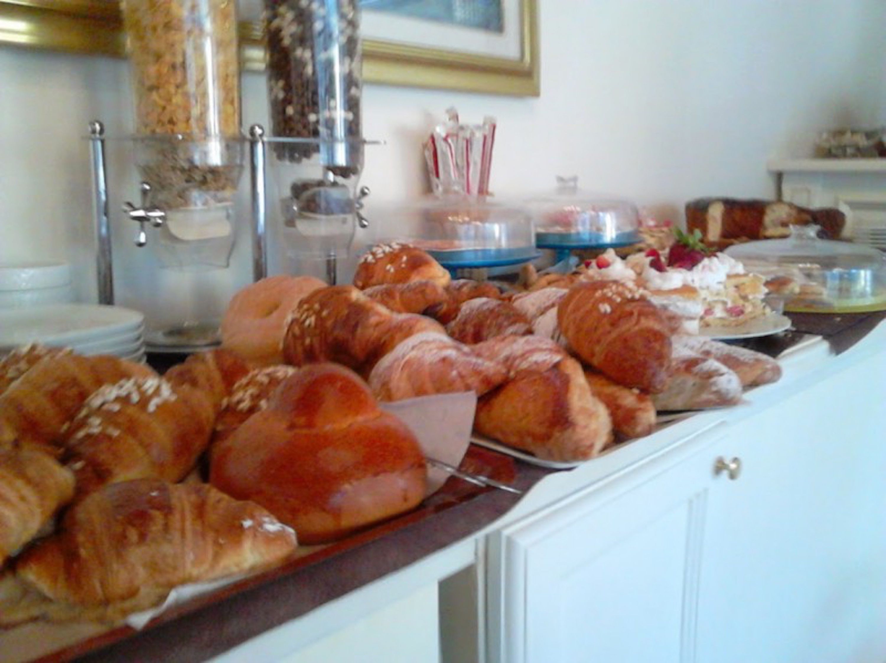 Un bufé con diversas opciones de panadería, incluyendo croissants y pasteles, y una máquina de café al fondo.