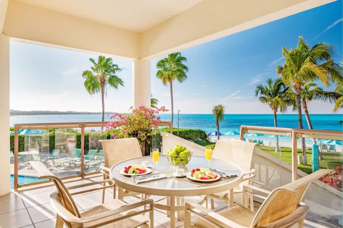 A balcony with a table set for dining, overlooking a pool and the ocean.