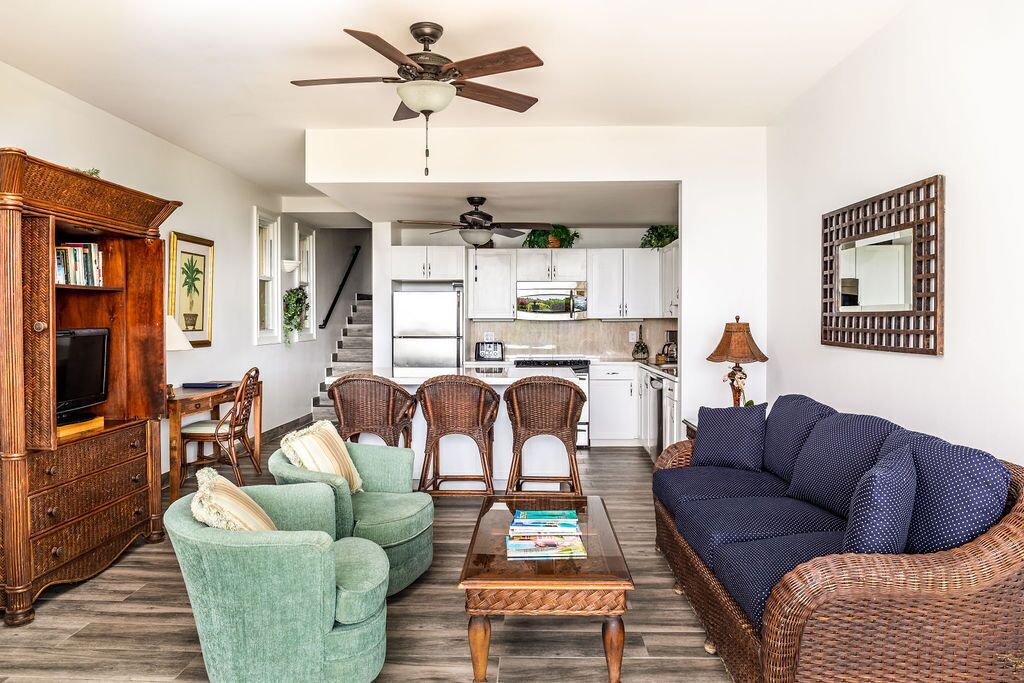 A living room with a green sofa, a blue sofa, a wooden coffee table, wicker chairs, and a television on a wooden cabinet.