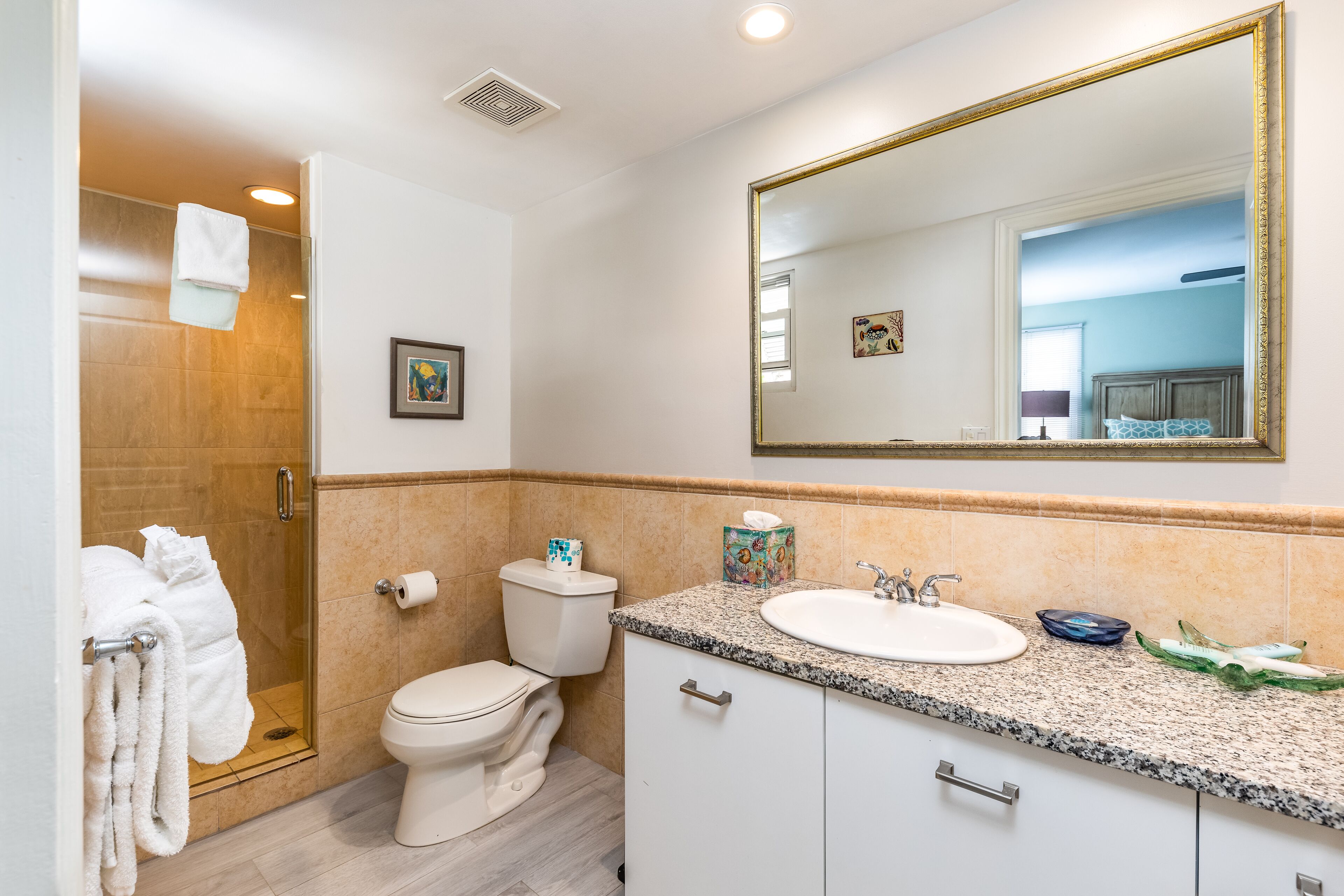 A bathroom with a glass shower enclosure, a toilet, a sink with a granite countertop, and a large mirror.