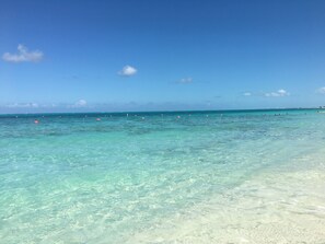 Vista despejada de una playa con aguas turquesas y algunos boyas anaranjadas.
