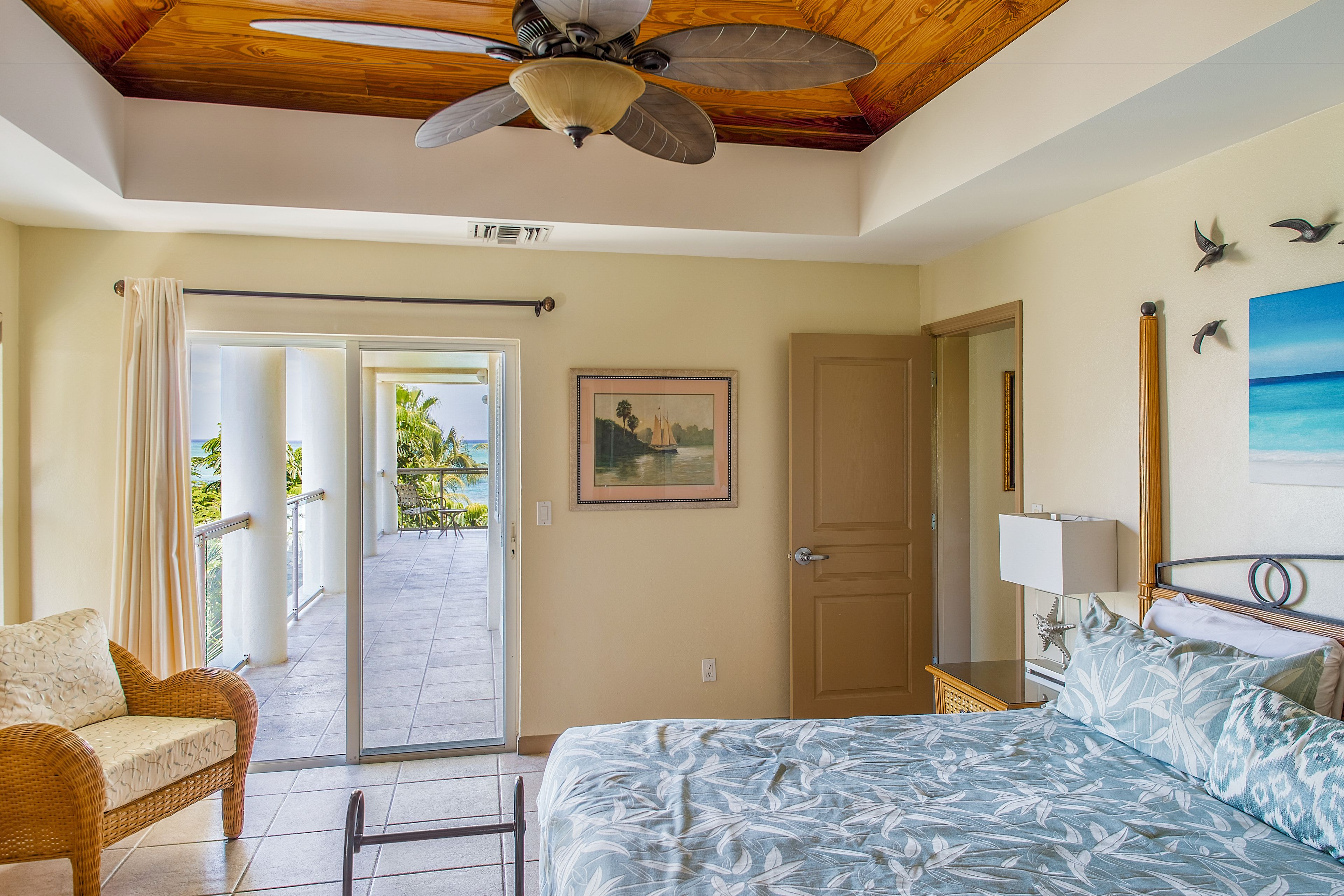 Une chambre à coucher avec un lit, un ventilateur de plafond, une porte, une fenêtre et un tableau accroché au mur.