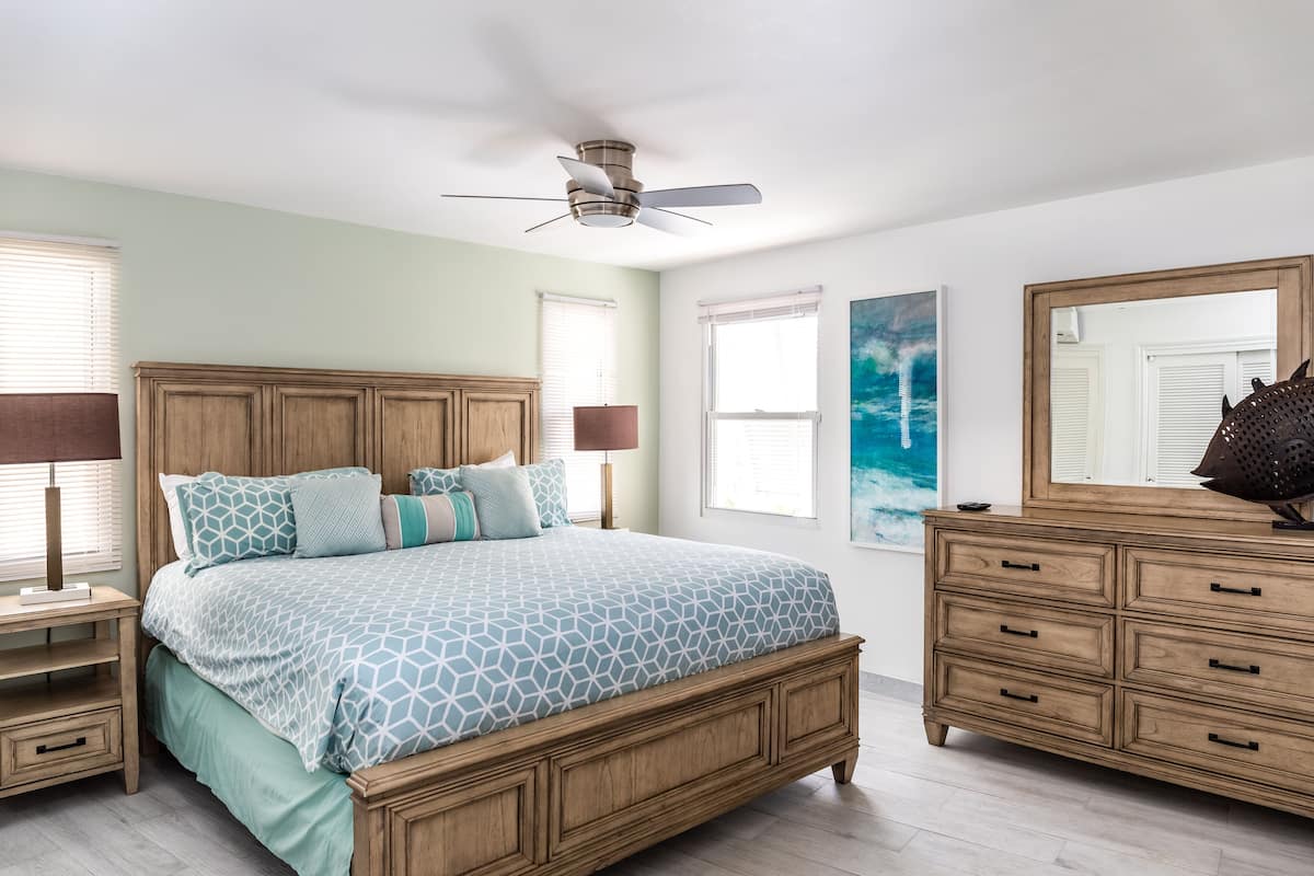 A bedroom with a wooden bed, bedside tables, a dresser, and a ceiling fan.