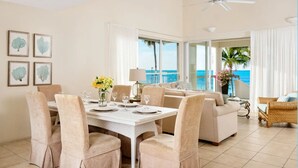 A dining area with a table set for four, a sofa, and a view of the ocean. - Coral Gardens on Grace Bay (Providenciales)