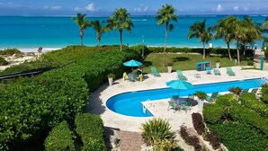 A pool area with lounge chairs and umbrellas, surrounded by palm trees and a view of the ocean. - Coral Gardens on Grace Bay (Providenciales)