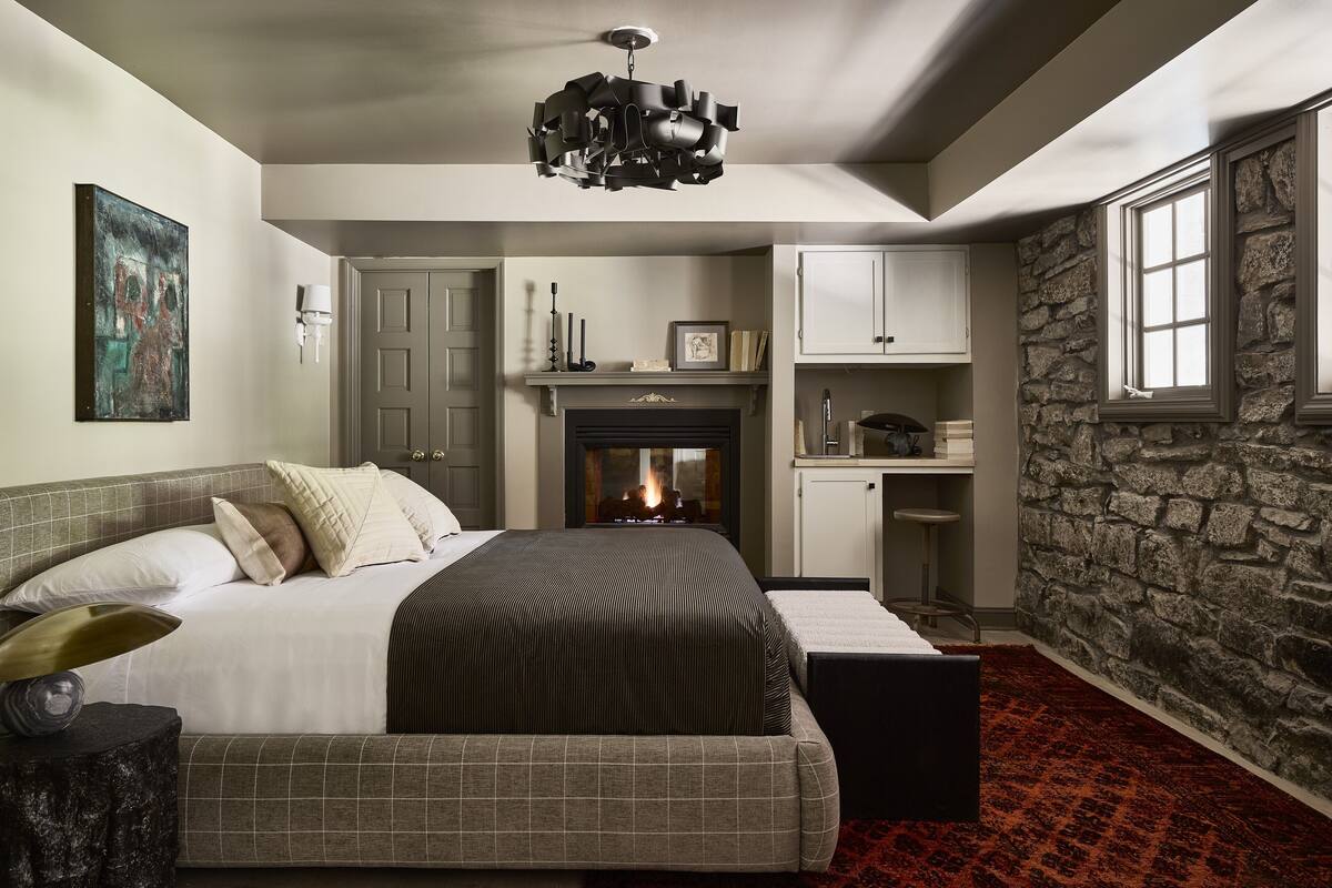 Une chambre avec un grand lit, une cheminée, un mur en pierre et une fenêtre.