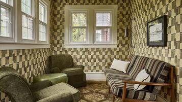 Een kamer met behang met een patroon, een groene fauteuil, een gestreepte bank en een ingelijst kunstwerk aan de muur.