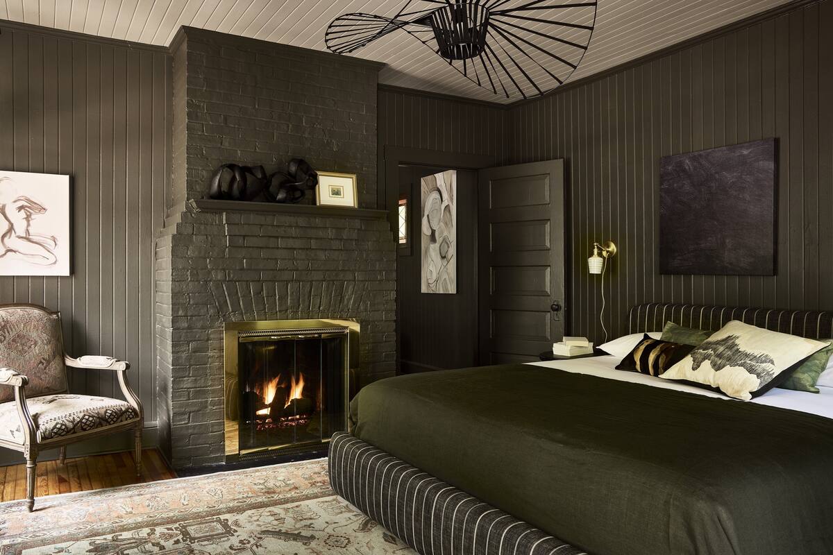 Une chambre avec une cheminée, un lit avec une literie verte, une chaise et un tapis.