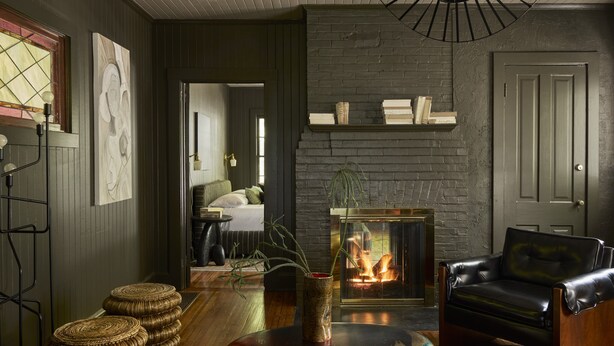 A cozy living room with a fireplace, leather armchair, and a stack of woven stools. - Blind Tiger Asheville (Asheville)