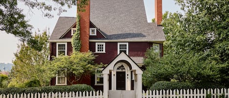A two-story house with a white picket fence, a brick chimney, and a dark red exterior.