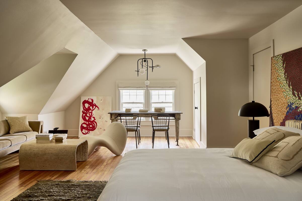 Une chambre de style loft moderne, avec un plafond en pente, un grand lit, un bureau avec deux chaises et une table à manger.