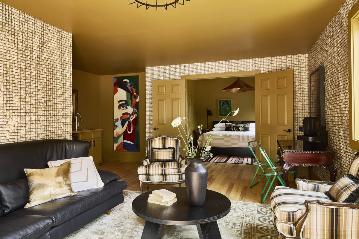 Un salon avec un canapé en cuir noir, un fauteuil à motifs écossais, une table basse ronde sur laquelle sont posés des livres, et un vase rempli de fleurs.