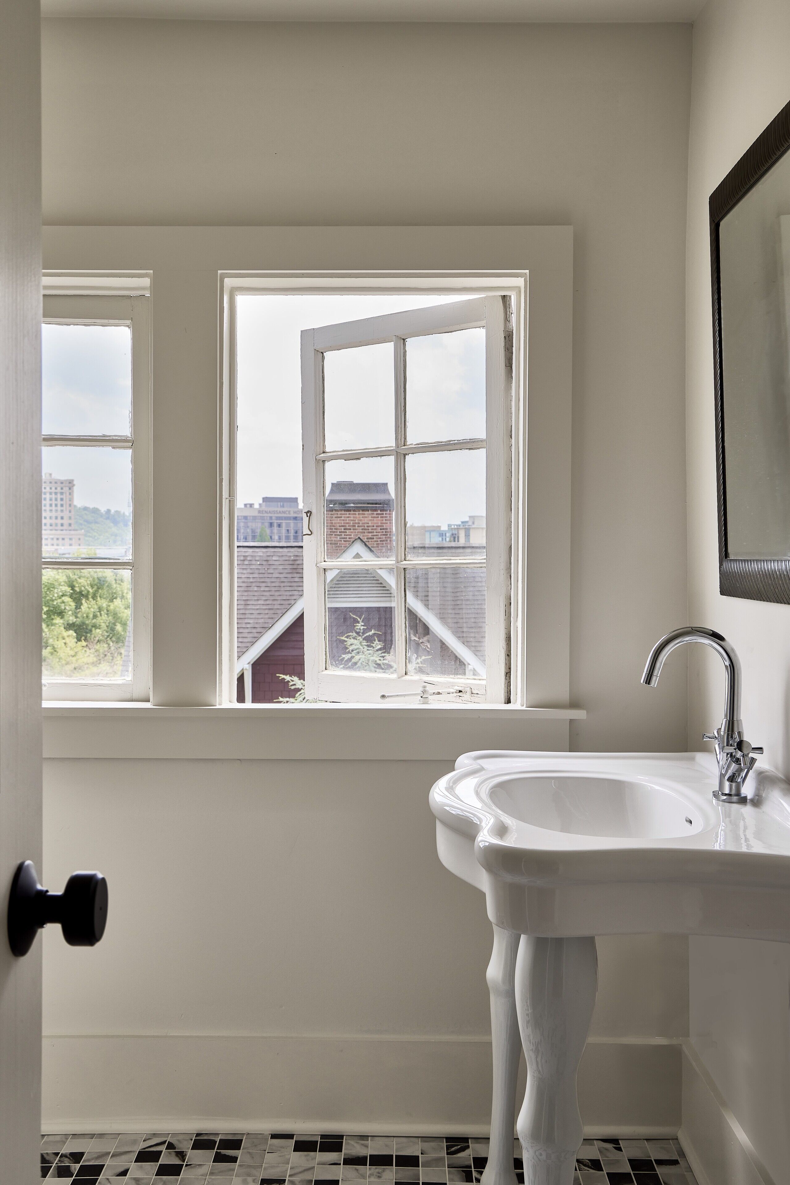 A bathroom with a white sink, a large window, and a view of buildings outside.