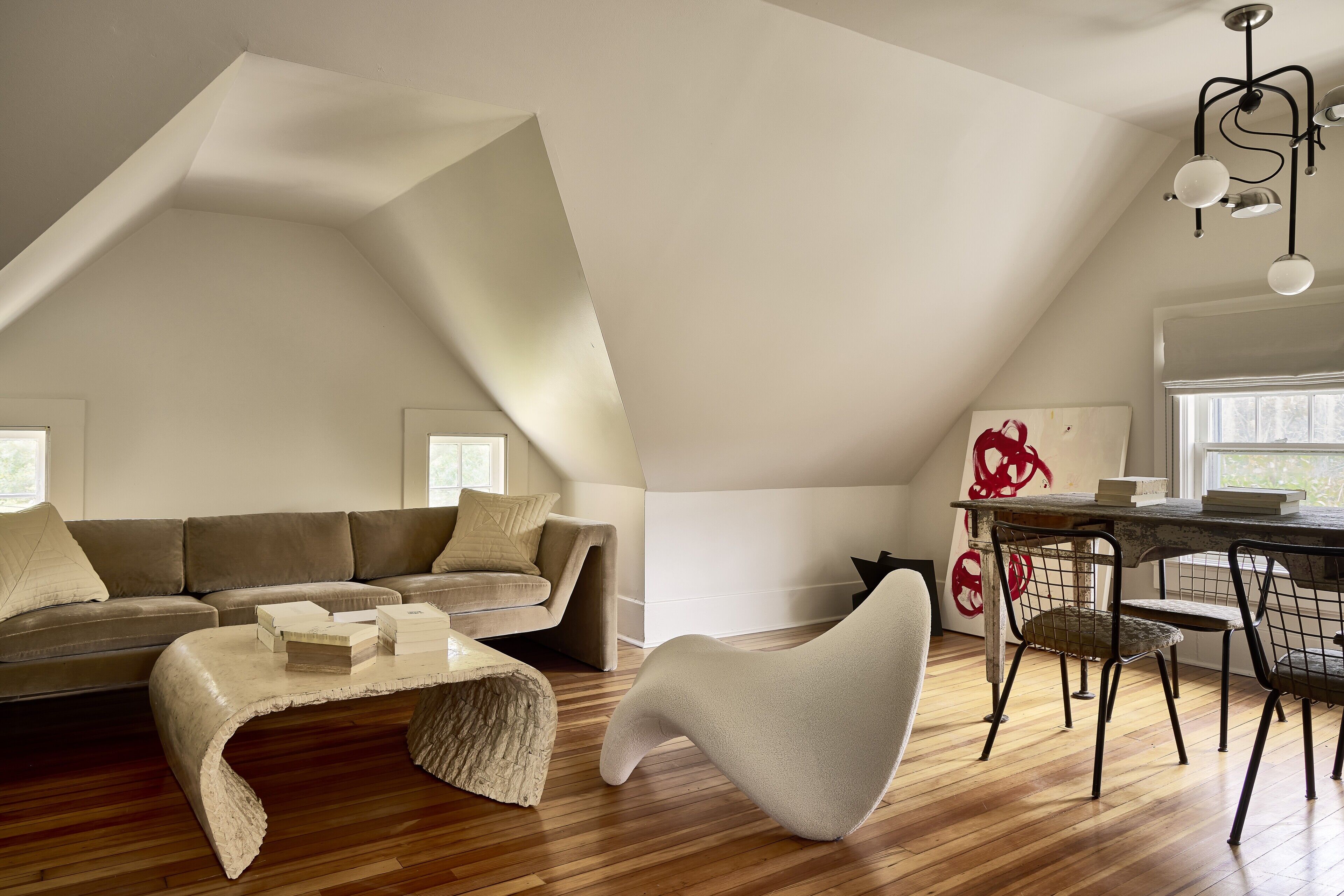 A loft-style living space with a sloped ceiling, a sofa, a coffee table, a dining table with chairs, and a modern chandelier.