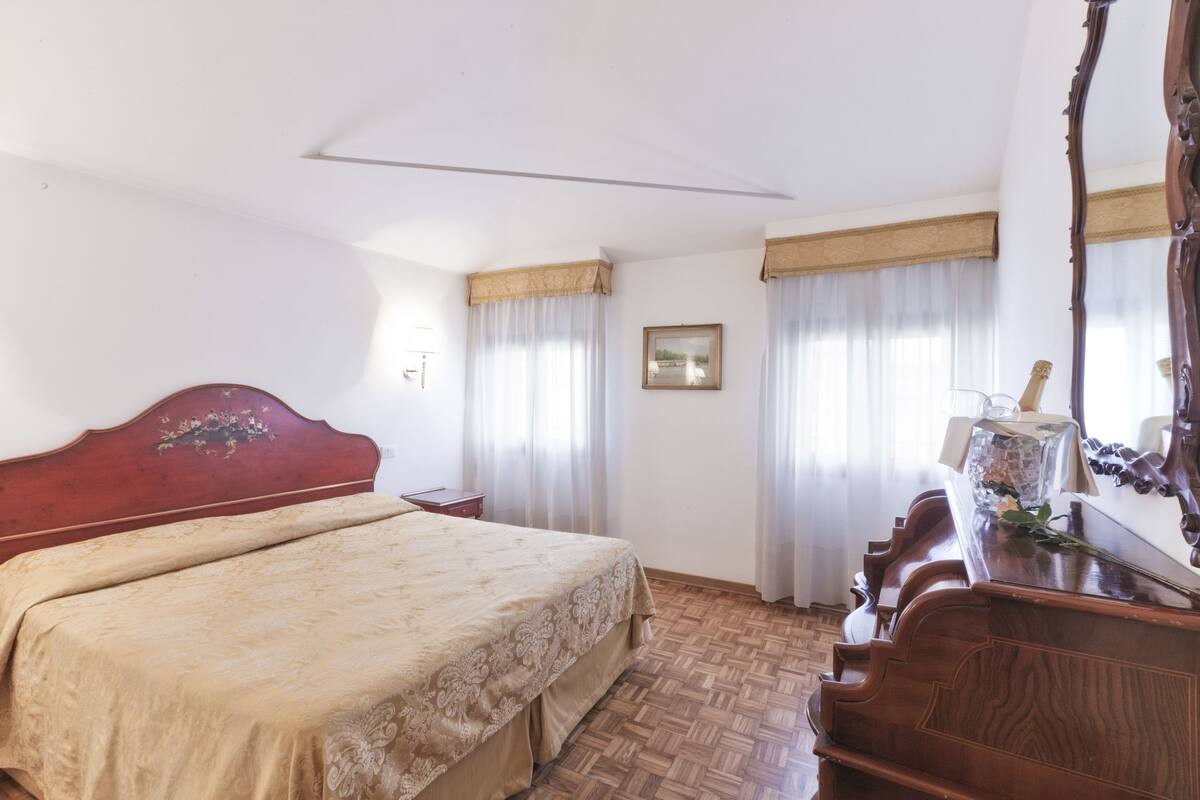 Een slaapkamer met een houten bed, een dressoir, een spiegel en een ingelijste foto aan de muur.