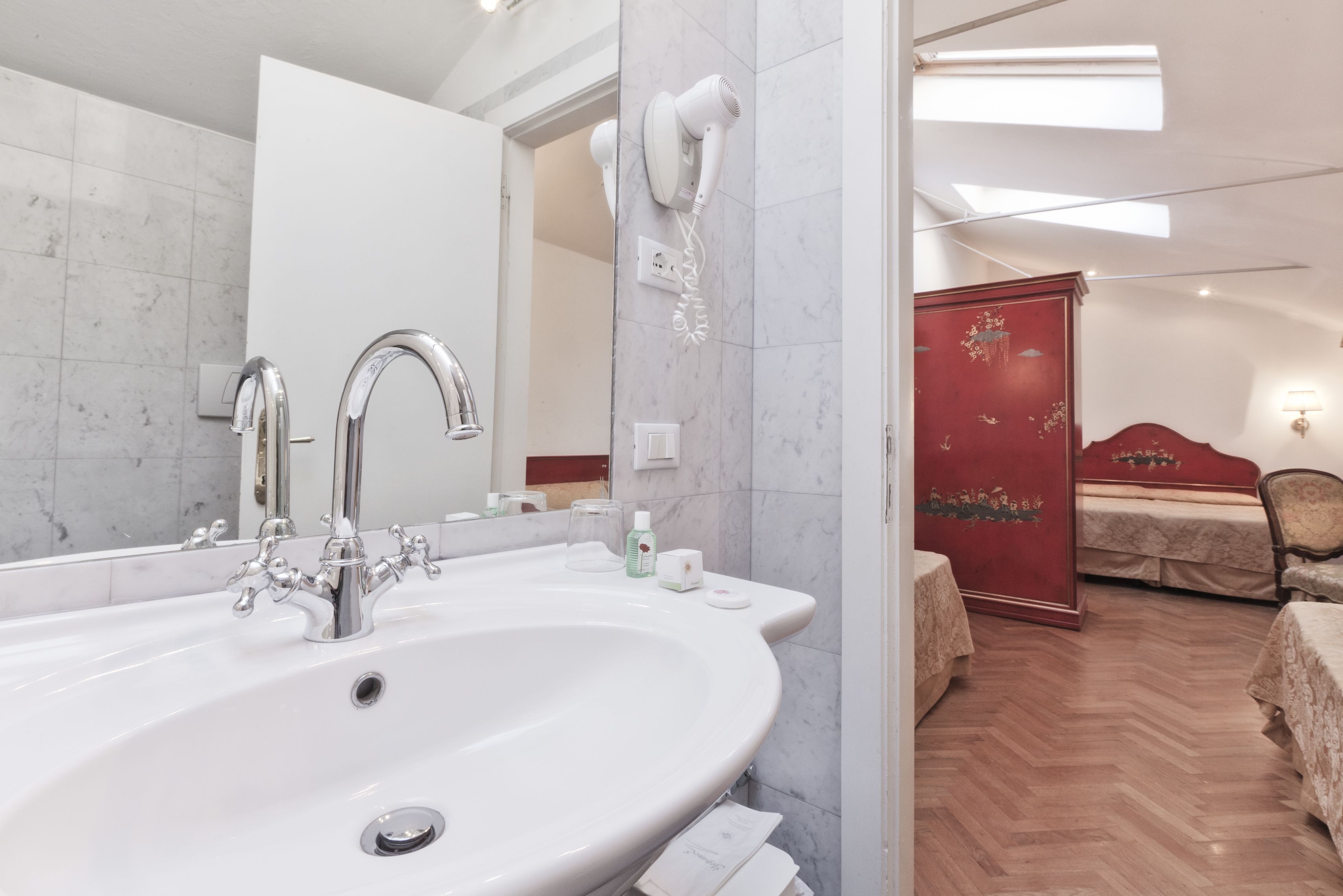 A bathroom with a large sink, a mirror, and a hairdryer mounted on the wall.