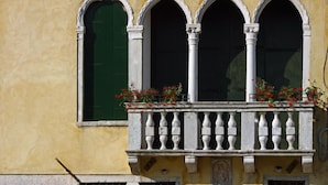 Fachada de edificio con tres ventanas arqueadas y un balcón con barandilla blanca.
