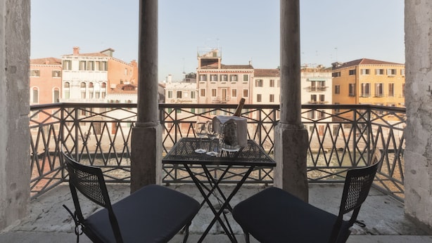 Un balcón con dos sillas y una mesa, con vista a un paisaje urbano de edificios históricos.