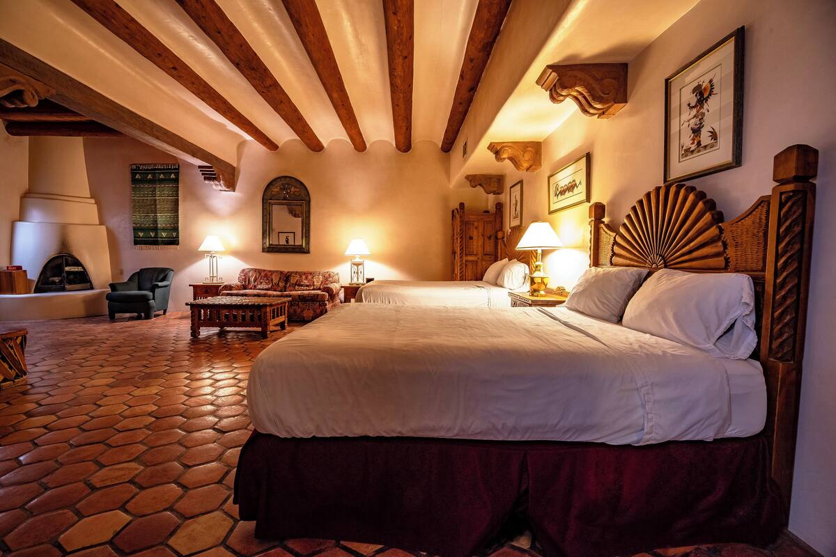 A spacious bedroom with a large bed, wooden beams, a tiled floor, and a fireplace.