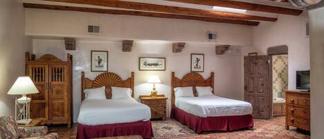 A room with two beds, a wooden wardrobe, a television, and a patterned rug.