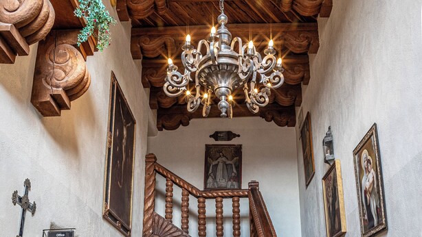 Un magnifique escalier en bois, agrémenté de rampes et surmonté d’un lustre, mène à un palier du deuxième étage, également doté d’une rampe en bois.