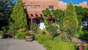 A building with a stucco exterior, a front porch, and a garden with various plants and flowers.