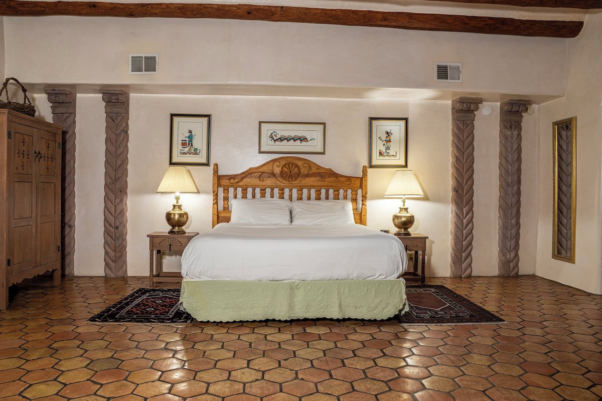 A bedroom with a large bed, two bedside tables with lamps, a wooden wardrobe, and a decorative headboard.