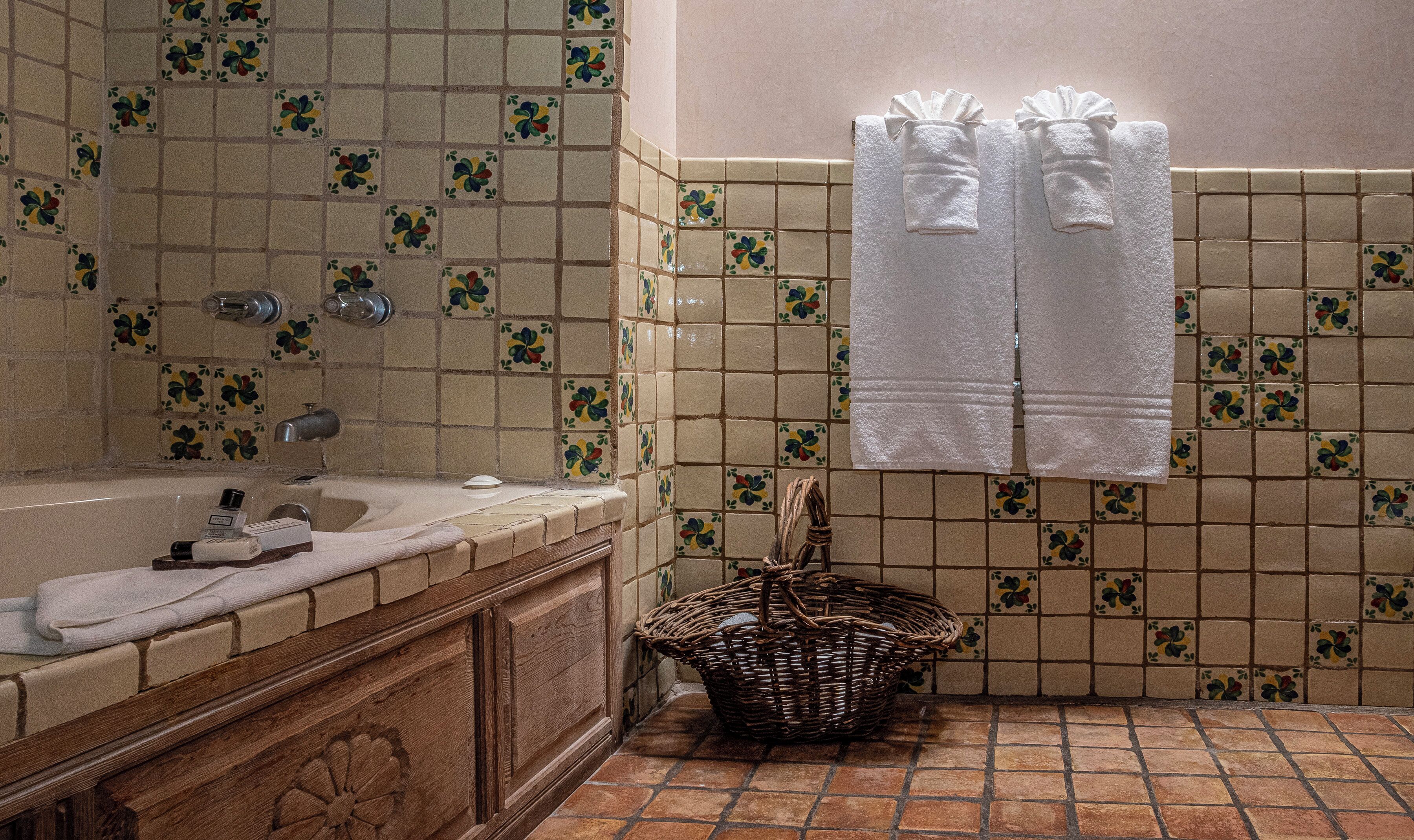 A bathroom with a bathtub, a sink, and a tiled shower area. There are towels hanging on the wall and a basket on the floor.