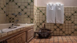 A bathroom with a bathtub, a sink, and a tiled shower area. There are towels hanging on the wall and a basket on the floor.