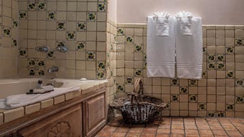 A bathroom with a bathtub, a sink, and a tiled shower area. There are towels hanging on the wall and a basket on the floor.