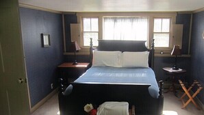 A bedroom with a large bed, two bedside tables, a small table, and a window with curtains. - Inn at Neshobe River (Brandon)