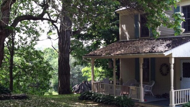 A two-story house with a porch, surrounded by trees. - Inn at Neshobe River (Brandon)