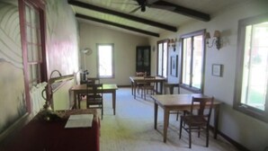 A room with a high ceiling, wooden beams, and a carpeted floor. There are several wooden tables and chairs arranged for dining. - Inn at Neshobe River (Brandon)