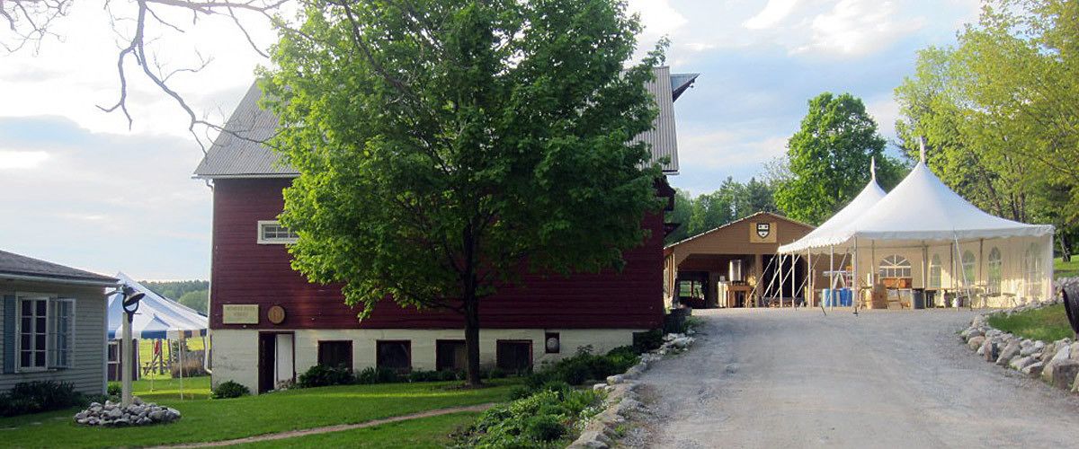 A red barn with a white facade, a gravel driveway, and a white tent structure.