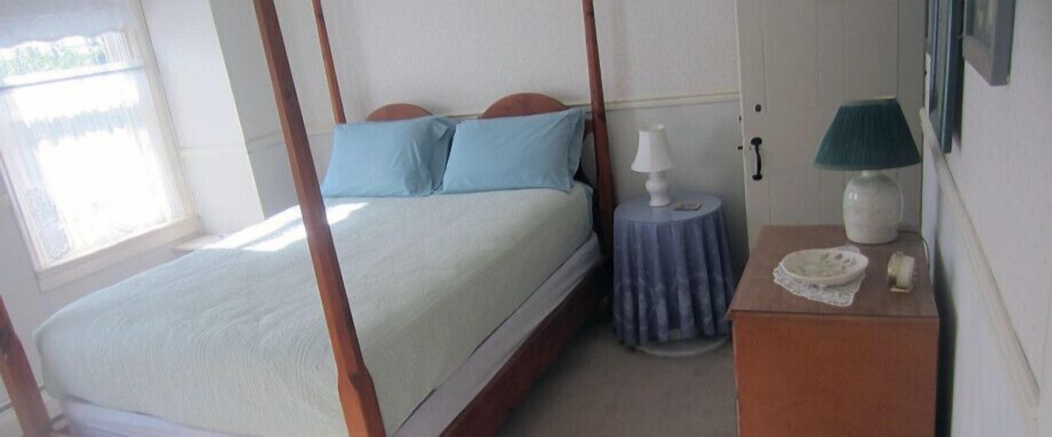 Un dormitorio con cama con dosel, una mesita de noche con lámpara y una pequeña mesa redonda con un plato.