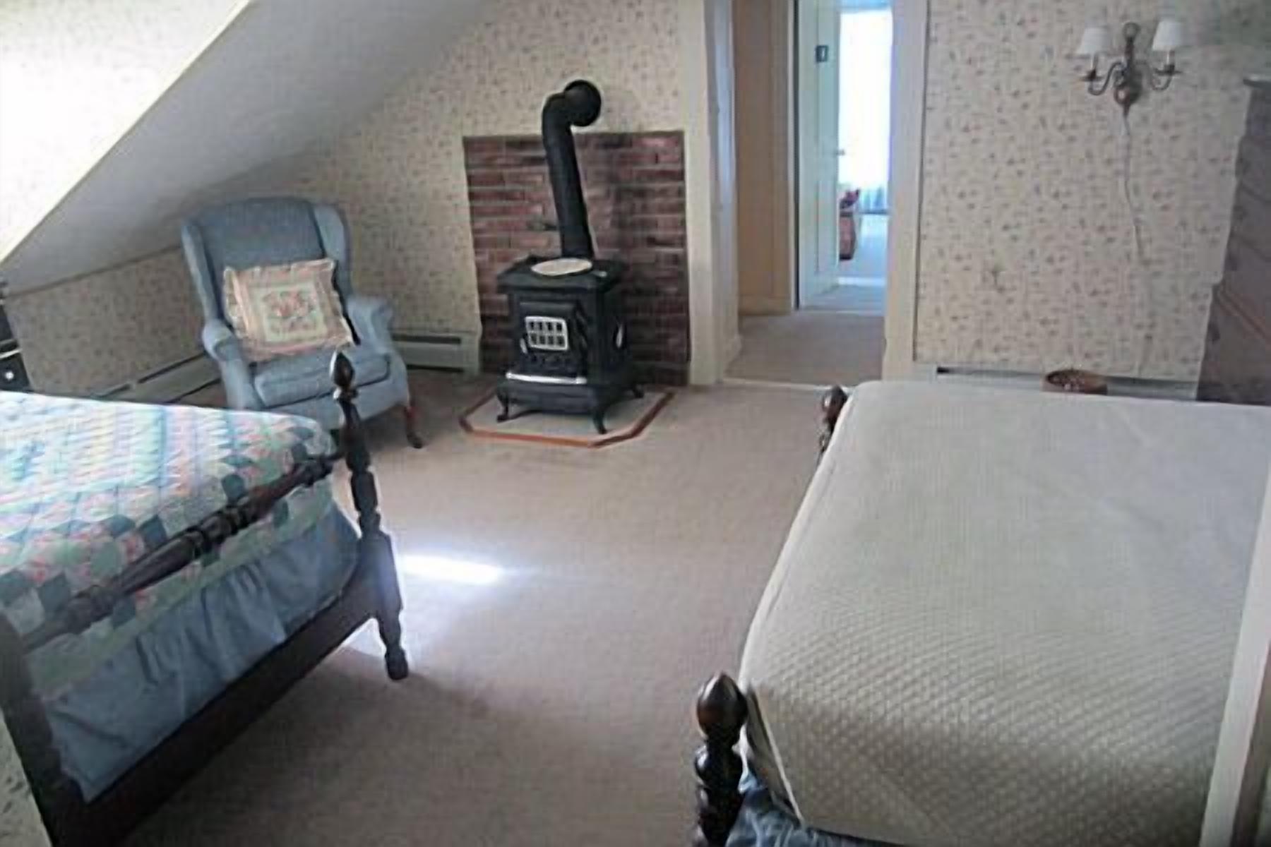 A bedroom with a bed, a chair, a fireplace, and a door leading to another room.