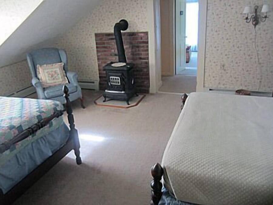A bedroom with a bed, a chair, a fireplace, and a door leading to another room.
