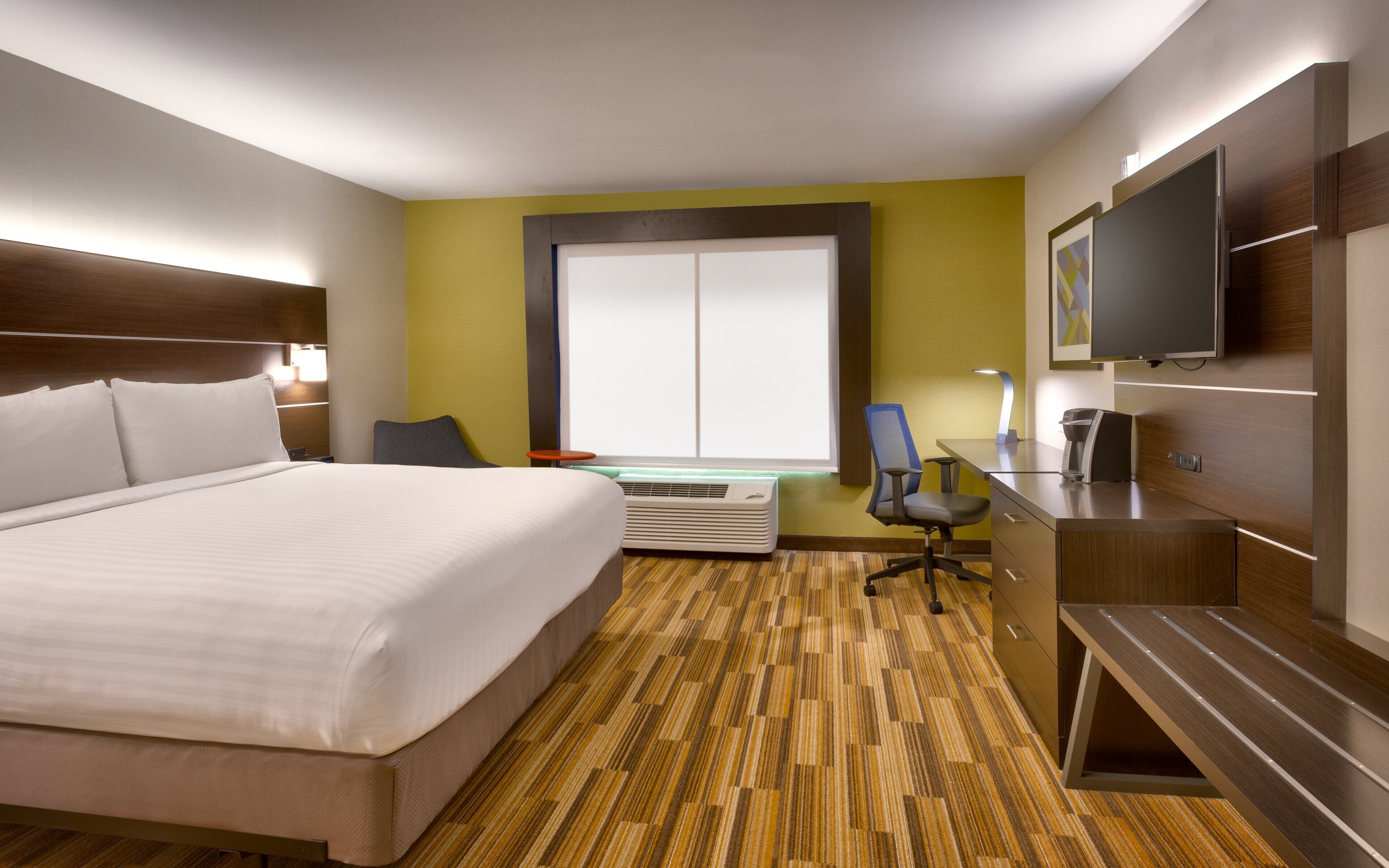 Een hotelkamer met een groot bed, een bureau met stoel, een televisie en een raam met zonwering.