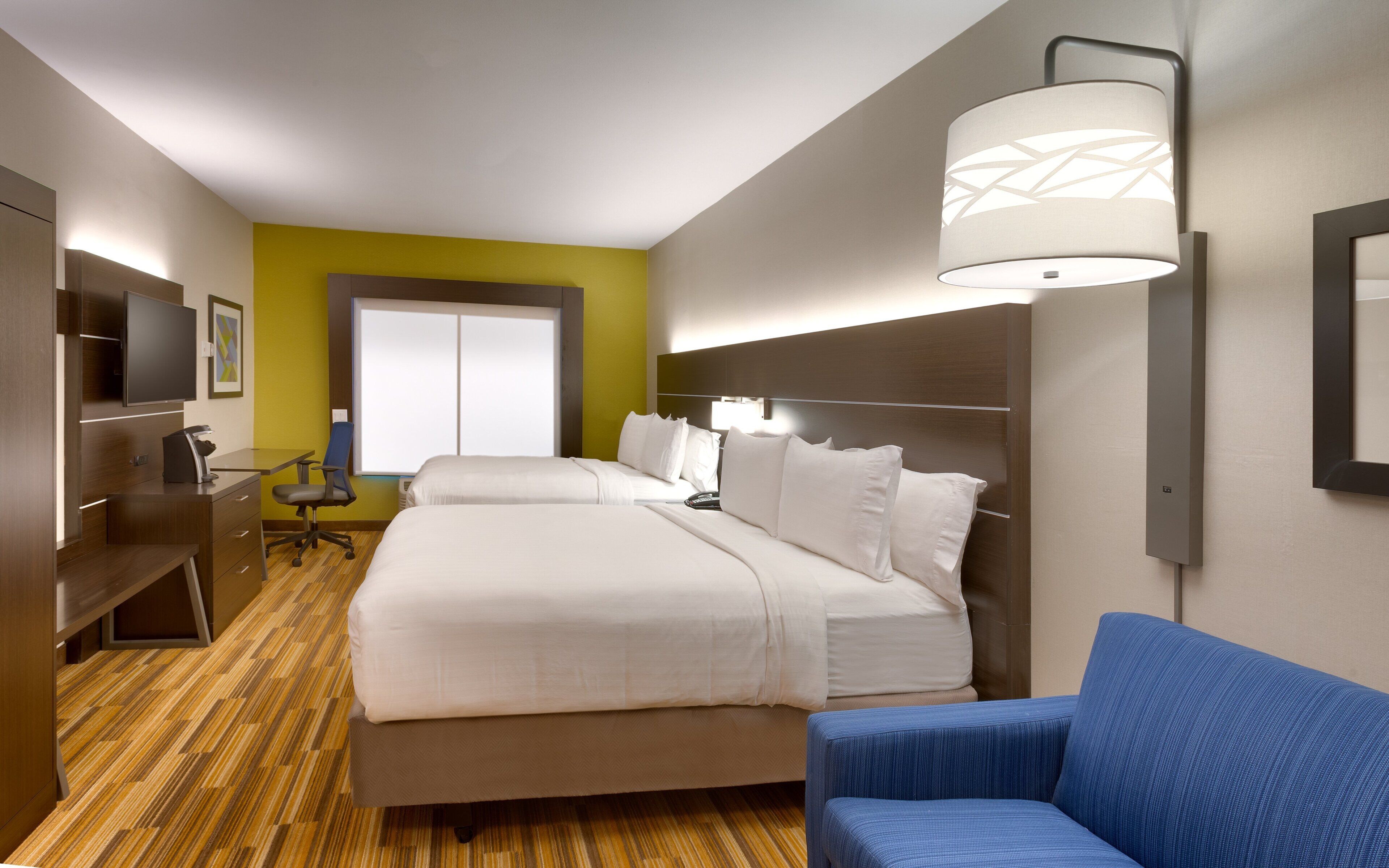 Habitación de hotel con una cama grande, un escritorio con silla, un televisor y una ventana con persianas.