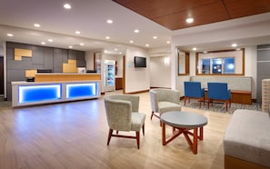 A hotel lobby with a reception desk, seating area, and a television mounted on the wall.