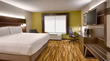 A hotel room with a large bed, a desk with a chair, a television, and a window with blinds.