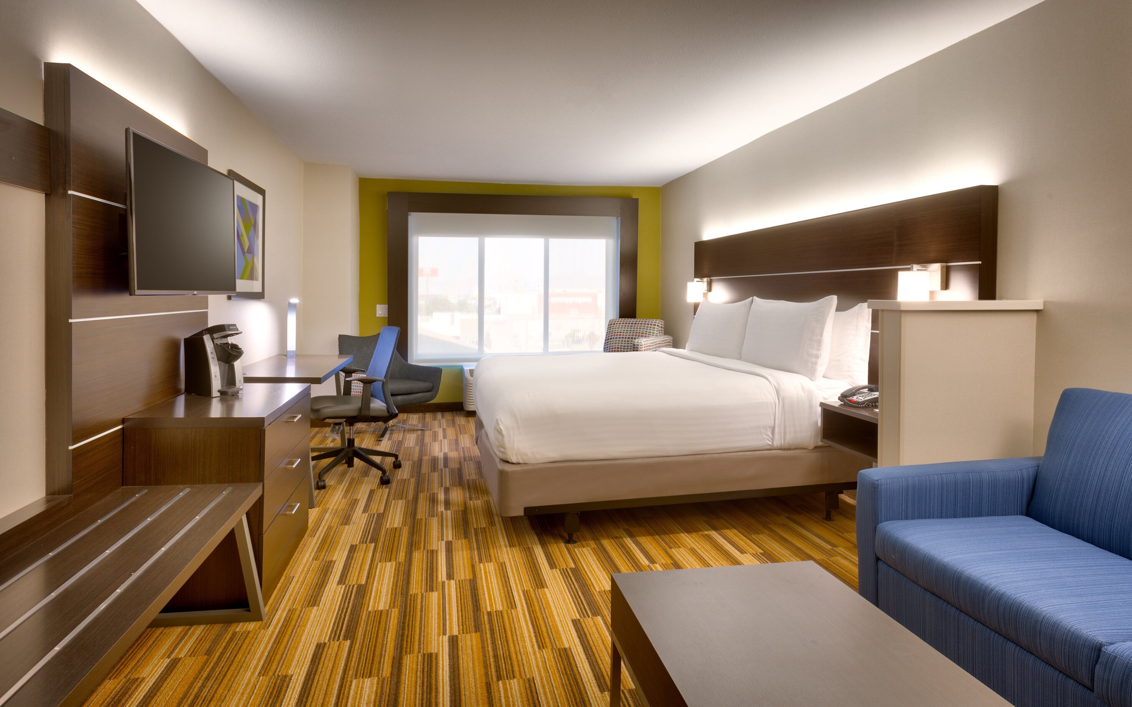 A hotel room with a bed, a desk, a chair, a television, and a window.